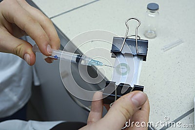 Contact lenses manufacturing. Worker hands stuffing form of lens with special amalgam using syringe. Editorial Stock Photo