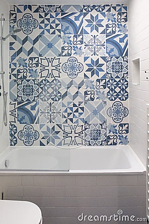 Bathroom with bath, toilet, niche in the wall and basin unit, with blue and white patchwork tiles above the bath. Stock Photo