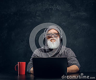 Contemporary elderly hacker with cup and laptop sitting at table Stock Photo