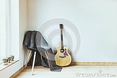 Contemporary home interior. Black chair covered with woolen gray blanket and acoustic guitar in front of an empty white wall. Stock Photo