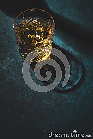 Contemporary still life with whiskey, scotch or bourbon glass with ice on textured blue background with hard lights and shadows, Stock Photo