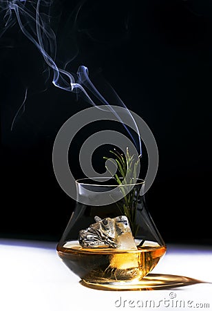 Contemporary still life with whiskey, scotch or bourbon glass with steaming rosemary, shard ice on black white background Stock Photo