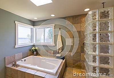 Contemporary upscale home spa bathroom interior with acrylic soaking tub , glass block shower, slate tile walls, and view windows Stock Photo