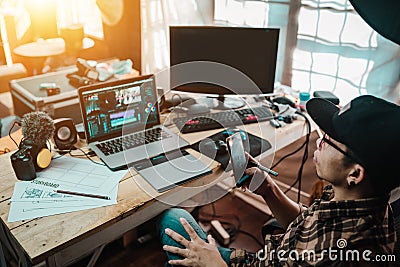 The content creator using mobile working with the laptop editing video footage in the house studio Stock Photo