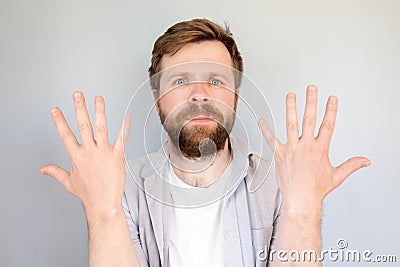 Contented, calm man in a shirt shows the number ten on fingers or his newly washed hands. Gray background. Stock Photo