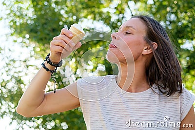 Contented woman eating ice cream, on a summer day. She licks lips with her tongue and savor the refreshing taste of a Stock Photo