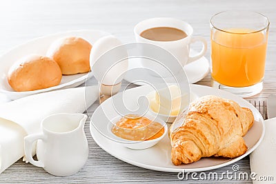 Continental breakfast with a croissant, boiled egg. Coffee or tea with milk, a glass of juice, buns, butter, jam Stock Photo