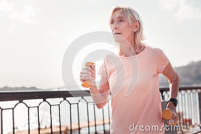 Concentrated aged woman doing exercise and holding dumbbells. Stock Photo