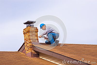 Contractor Builder on roof with blue hardhat caulking chimney Stock Photo