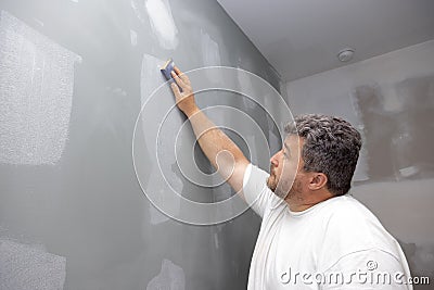 A contractor is sanding the wall after putting up putty as part of a renovation project for an apartment Stock Photo