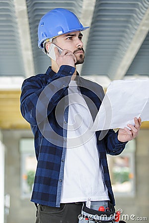 contractor on site holding plans and making telephone call Stock Photo