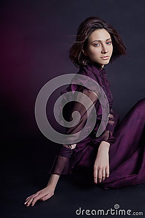 Contrast fashion Armenian woman portrait with big blue eyes sit on a dark background in a purple dress. Lovely gorgeous girl Stock Photo