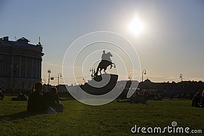 Contrast shot of people sitting on grass in Alexander Garden park with silhouette of Bronze Horseman sculpture of Peter the Great Editorial Stock Photo