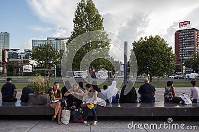 Contrast between three european girls, friends, sitting in short and summer clothing while a group of muslim women is sat behind Editorial Stock Photo