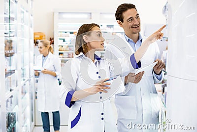 Male and female pharmacists positively discussing assortment of medicines. Stock Photo