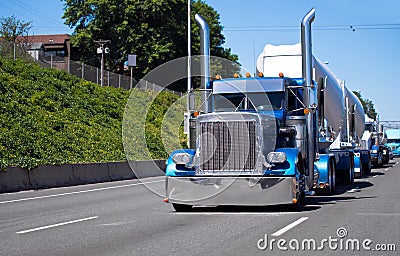 Convoy of big rigs semi trucks on the road with blue classic American bonnet semi tractor with bulk trailer Stock Photo