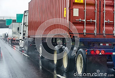 Convoy of different big rig semi truck with commercial cargo in semi trailers and container running on the wet raining highway Stock Photo