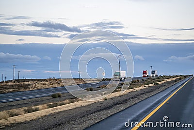 Convoy of different big rigs semi trucks with semi trailers driving on the divided straight highway road at twilight Stock Photo