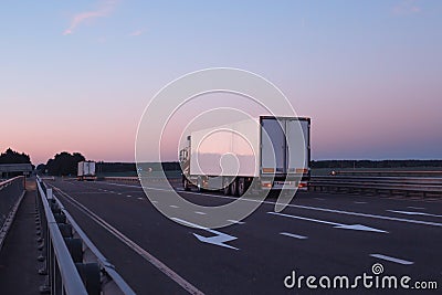 A convoy of trucks trucks transports the cargo in the evening on the highway, the concept of logistics and freight, copy Stock Photo