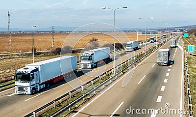 Convoy of White transportation trucks in line on a countryside highway Stock Photo