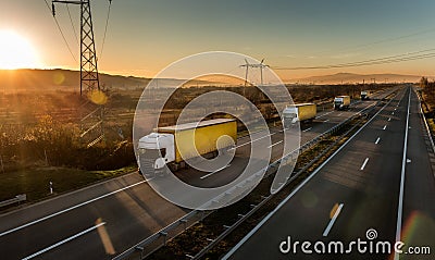 Convoy of white transportation trucks with yellow trailers in line on a country highway at sunset Stock Photo