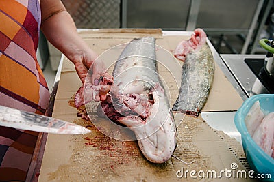 The cook cuts a large fish on the table with a knife Stock Photo