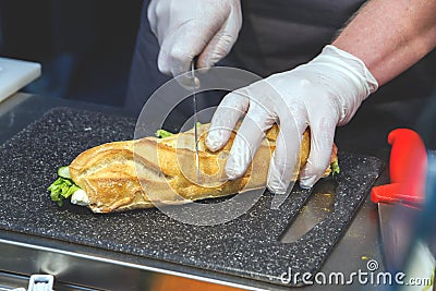 Cook in disposable gloves cuts sandwich Stock Photo