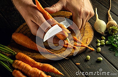 The cook hands with a knife peel the carrots on kitchen cutting board to prepare a vegetable meal Stock Photo