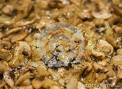Mushrooms and onion sliced cooking on a black hot frying pan. Stock Photo