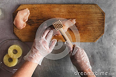 Cook prepares chicken on a wooden cutting board, hands, chicken, pineapple, gloves. meat tenderizer. recipe for chicken Stock Photo