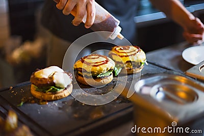 Cook preparing burger adding the sauce on the cream cheese. Stock Photo