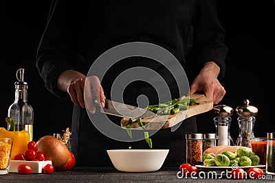 Cook preparing food by the chef, the cook cuts green beans on a background of vegetables. Black background for design, vegetation Stock Photo