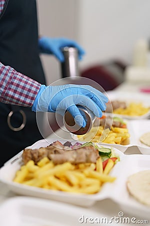 Cook seasoning Greek kalamaki with pepper on a kitchen counter. Chef preparing traditional Mediterranean fast food for take away Stock Photo