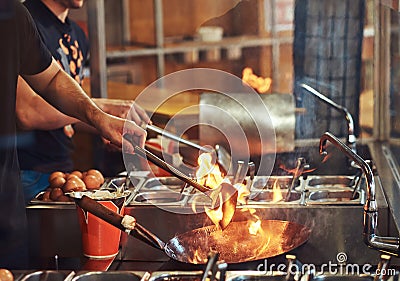 Cooking process in an Asian restaurant. Cook is stirring vegetables in a wok on a flame. Stock Photo