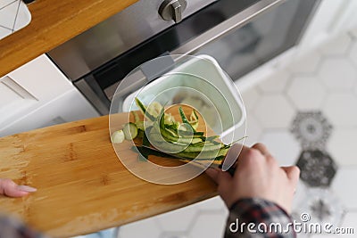 Cook throwing cucumber peels in a bokashi container for decomposition. Female person recycling organic food waste in a compost bin Stock Photo