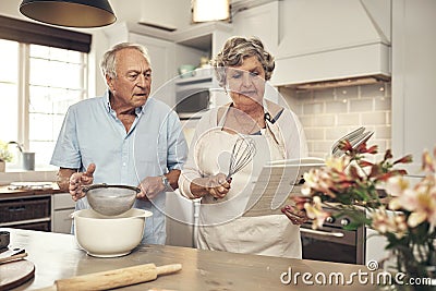 Cookbooks make baking so much easier. a senior couple baking together at home. Stock Photo