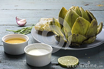 Cooked artichoke with dips and bread on rustic gray blue wood Stock Photo