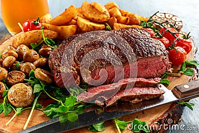 Cooked Beef Ribeye Steak with Potato, Mushrooms, tomatoes on wooden board. Stock Photo