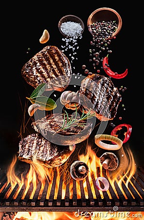 Cooked beef steaks with vegetables and spices fly over the blazing grill barbecue fire Stock Photo