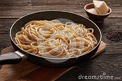 Cooked cacio pepe pasta in a skillet with pecorino cheese on wooden background Stock Photo