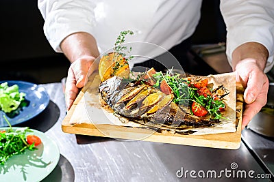 Cooked dorado with vegetables in the hands of chef Stock Photo