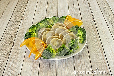 Cooked gyozas stuffed with pork accompanied by pieces of broccoli boiled al dente and orange slices Stock Photo