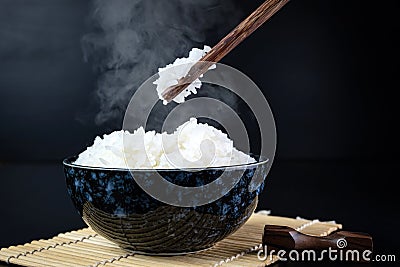 Cooked jasmine rice in ceramic cups and chopsticks holding hot jasmine rice. Placed on a black wooden table. Close up shot Stock Photo