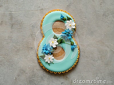 Cookie covered with blue glaze made in a form of number eight with flowers - cornflowers and daisies - on gray background. Ginger Stock Photo