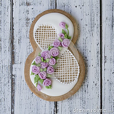 Cookie covered with glaze made in a form of number eight with sring flowers on white wooden background. Ginger biscuits Stock Photo