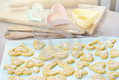 Cookies lying on a baking sheet. Kitchen utensils in the background, forms for cookies, rolling pin, whisk. Preparing Stock Photo