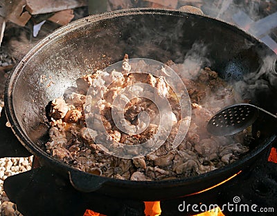 Cooking in a cauldron on open air on a summer day. Roasting meat in kazan over a fire. Traditionally a way of cooking. Stock Photo