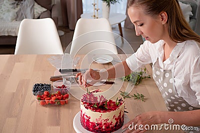 Cooking and decoration of cake with cream. Young woman pastry chef in the kitchen decorating red velvet cake Stock Photo