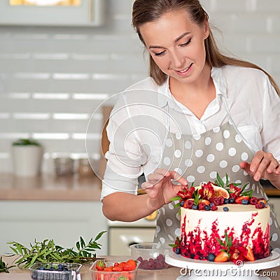 Cooking and decoration of cake with cream. Young woman pastry chef in the kitchen decorating red velvet cake Stock Photo