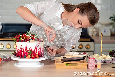 Cooking and decoration of cake with cream. Young woman pastry chef in the kitchen decorating red velvet cake Stock Photo